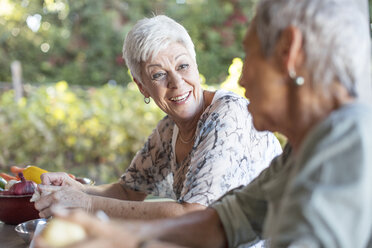 Portrait of smiling senior woman listening to her friend on terrace while preparing lunch - ZEF13837