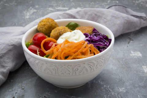 Lunch bowl of leaf salad, red cabbage, tomatoes, carrots, Falafel and yoghurt sauce stock photo