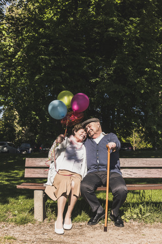 Happy senior couple with balloons sitting on bench in a park stock photo