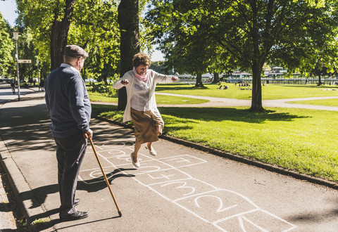 Senior woman playing hopscotch while husband watching her stock photo