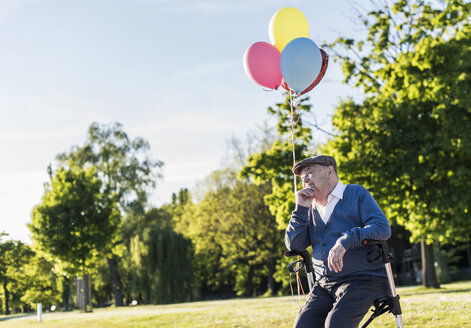 Nachdenklicher älterer Mann mit Luftballons, der auf seinem Rollator in der Natur sitzt - UUF10668