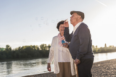 Älterer Mann bläst Seifenblasen am Strand bei Sonnenuntergang - UUF10675