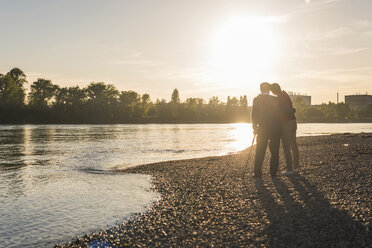 Back view of senior man and his adult daughter standing on the beach watching sunset - UUF10677