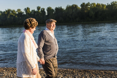 Glückliches älteres Paar spaziert Hand in Hand am Flussufer - UUF10682