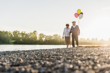 Senior couple with balloons strolling at riverside - UUF10684