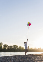 Ältere Frau mit Luftballons am Strand bei Sonnenuntergang - UUF10687