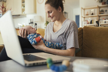 Mutter hält ihr neugeborenes Baby zu Hause neben dem Laptop - MFF03582