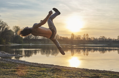 Germany, Bavaria, Feldkirchen, man doing parkour at lakeshore - KDF00733