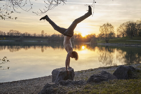 Germany, Bavaria, Feldkirchen, man doing a handstand at lakeshore - KDF00735