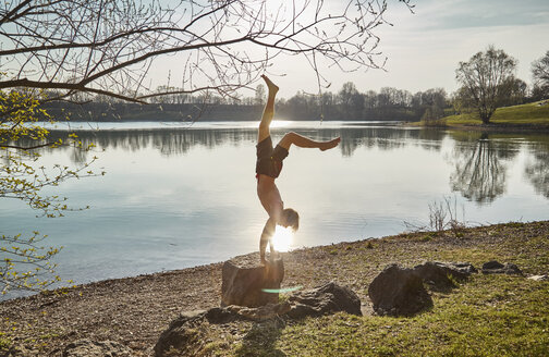 Germany, Bavaria, Feldkirchen, man doing a handstand at lakeshore - KDF00738