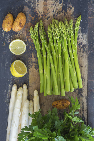 Grüner und weißer Spargel, Kartoffeln, geschnittene Zitrone und glatte Petersilie auf Holz, lizenzfreies Stockfoto