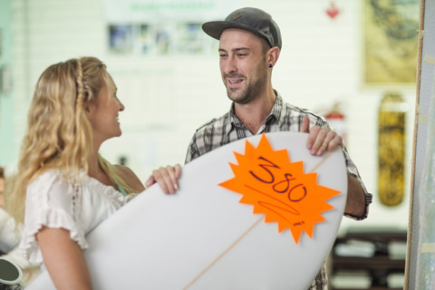 Verkäuferin zeigt Kunden die Preise für Surfbretter, lizenzfreies Stockfoto