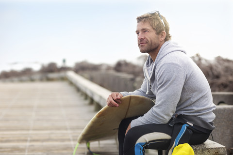 Mann sitzend mit Surfbrett am Strand, lizenzfreies Stockfoto