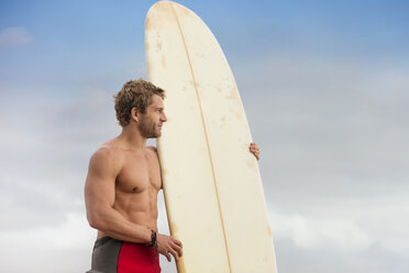 Mann steht am Strand mit Surfbrett und genießt die Aussicht - ZEF13874