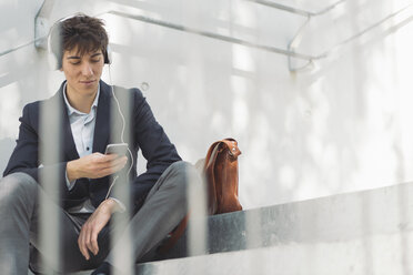 Young man in suit sitting on stairs listening to music - SKCF00307