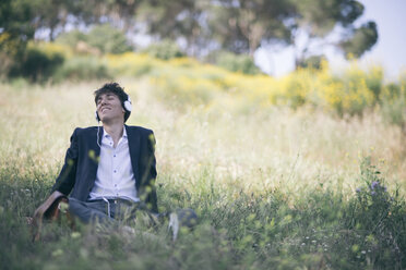 Young man in suit sitting on meadow listening to music - SKCF00308