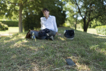 Young man sitting on meadow in park with cell phone away from him - SKCF00309