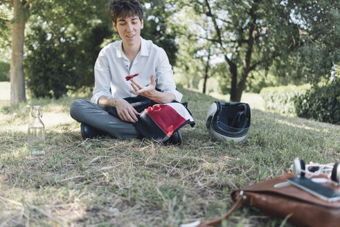 Junger Mann sitzt auf einer Wiese im Park und benutzt einen Fidget Spinner - SKCF00310