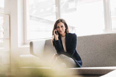 Porträt einer lächelnden Geschäftsfrau mit Mobiltelefon auf einer Couch - JOSF00956