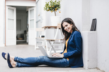 Lächelnde Geschäftsfrau mit Laptop auf dem Boden - JOSF00962