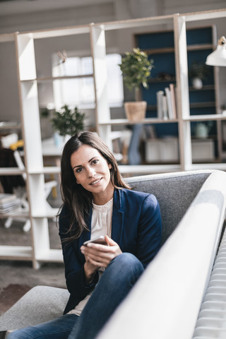 Porträt einer selbstbewussten Geschäftsfrau mit Mobiltelefon auf einer Couch, lizenzfreies Stockfoto