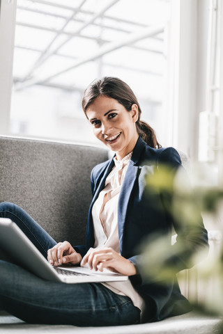Porträt einer lächelnden Geschäftsfrau mit Laptop auf einer Couch, lizenzfreies Stockfoto