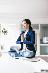 Businesswoman sitting on table meditating - JOSF00970