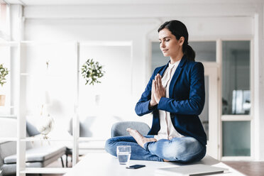 Businesswoman sitting on table meditating - JOSF00971