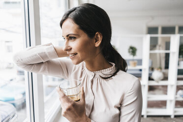 Smiling woman holding glass looking out of window - JOSF00987