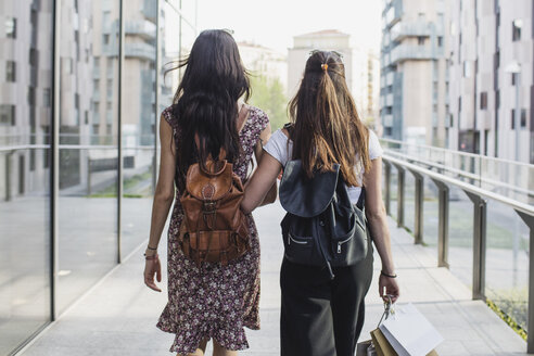 Zwei junge Frauen mit Rucksäcken und Einkaufstaschen gehen in der Stadt spazieren - MRAF00185