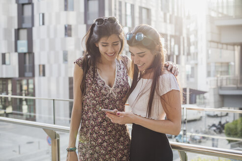 Zwei lächelnde junge Frauen schauen auf ein Handy in der Stadt - MRAF00186