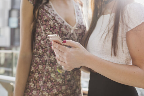Zwei junge Frauen teilen sich ein Mobiltelefon in der Stadt - MRAF00188