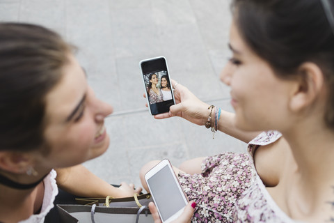 Zwei junge Frauen schauen sich Fotos auf dem Handy an, lizenzfreies Stockfoto