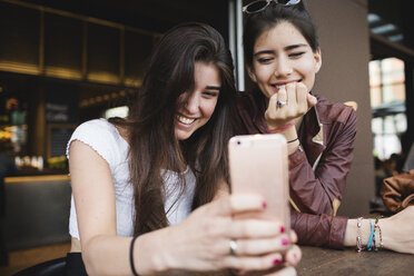 Zwei glückliche junge Frauen schauen auf ihr Handy in einer Bar - MRAF00202