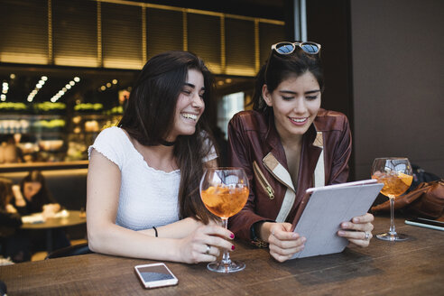 Zwei glückliche junge Frauen schauen sich in einer Bar ein Tablet an - MRAF00206