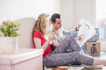 Young couple in new home sitting on floor discussing ground plan - UUF10701