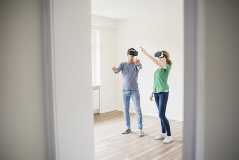 Junges Paar, das in einer leeren Wohnung mit VR-Brille diskutiert - UUF10709