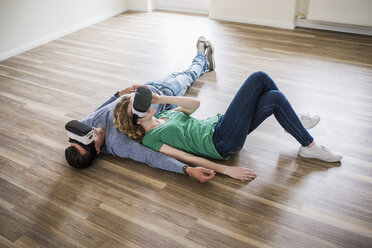 Young couple lying on floor in empty apartment wearing VR glasses - UUF10710