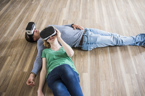 Junges Paar liegt auf dem Boden in einer leeren Wohnung und trägt eine VR-Brille, lizenzfreies Stockfoto