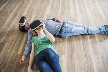 Young couple lying on floor in empty apartment wearing VR glasses - UUF10711