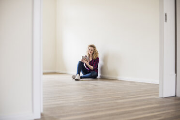 Junge Frau in neuer Wohnung sitzt auf dem Boden und benutzt ein Tablet - UUF10716