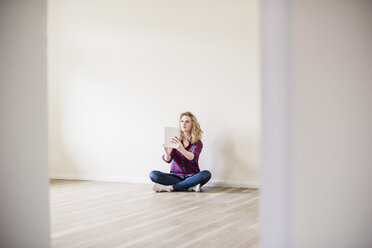Junge Frau in neuer Wohnung sitzt mit Tablet auf dem Boden - UUF10717