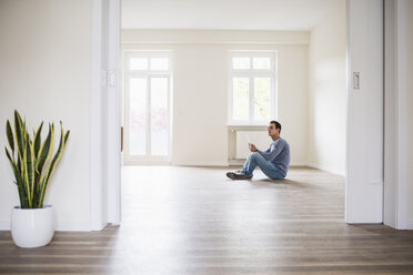 Young man in new home sitting on floor with tablet - UUF10724