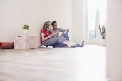 Young couple in new home sitting on floor with tablet stock photo