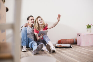 Young couple in new home sitting on floor with tablet - UUF10730