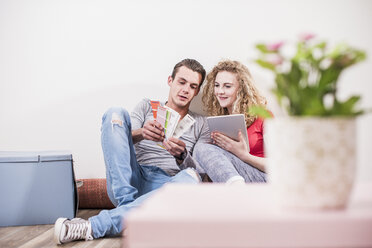 Junges Paar in einem neuen Haus, das mit einem Tablet auf dem Boden sitzt und ein Farbmuster auswählt - UUF10732