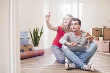 Young couple in new home sitting on floor with tablet - UUF10734