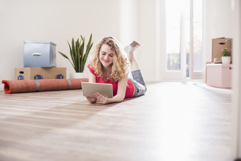 Junge Frau in neuer Wohnung mit Tablet auf dem Boden liegend, lizenzfreies Stockfoto