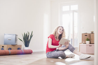 Junge Frau in neuer Wohnung sitzt mit Tablet auf dem Boden - UUF10738
