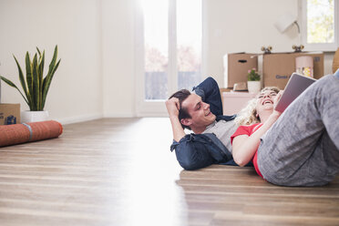 Glückliches junges Paar in neuer Wohnung mit Tablet auf dem Boden liegend - UUF10739
